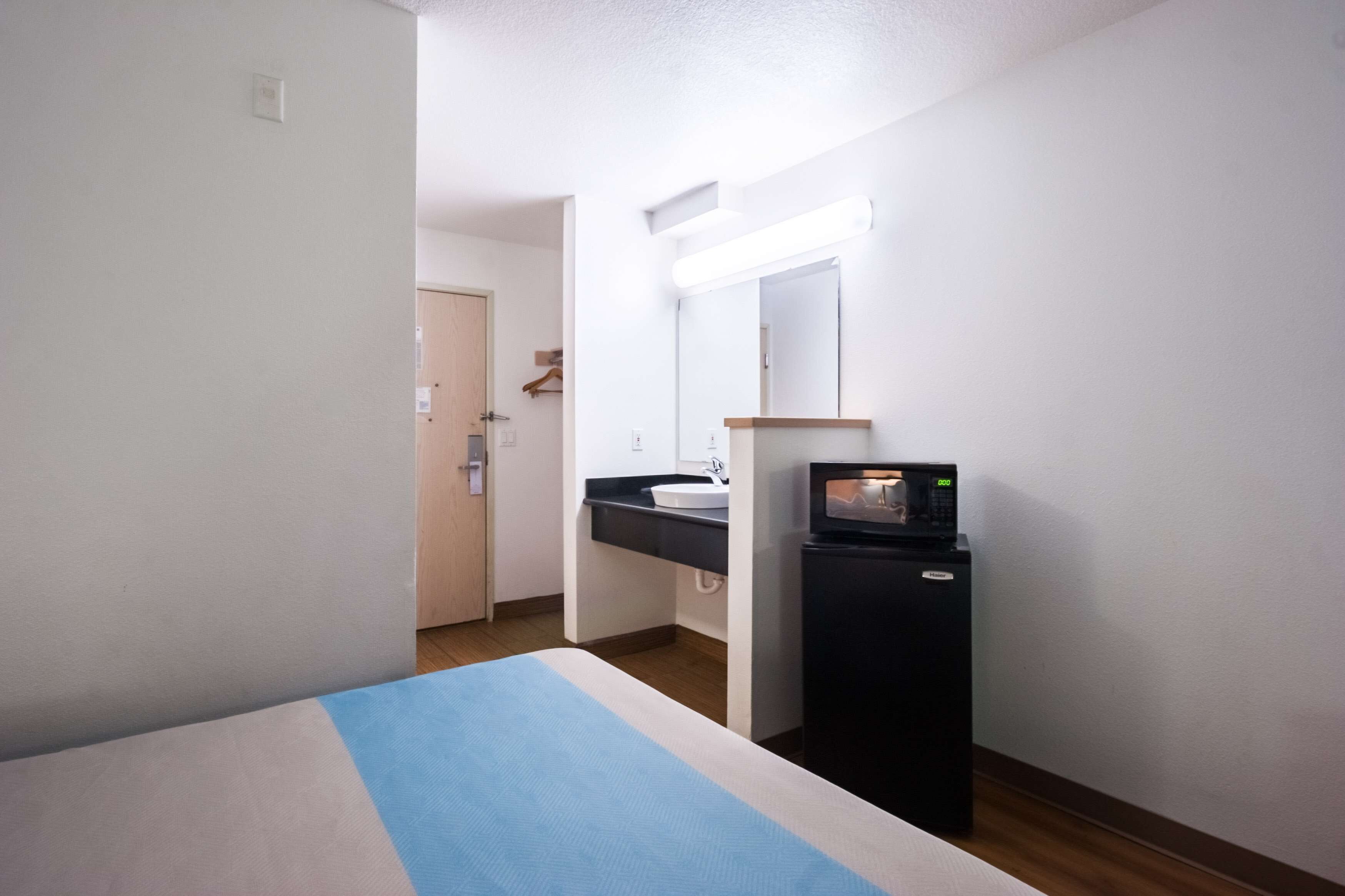 A hotel room with a bed, a small kitchenette with a microwave, a sink, and a mirror.