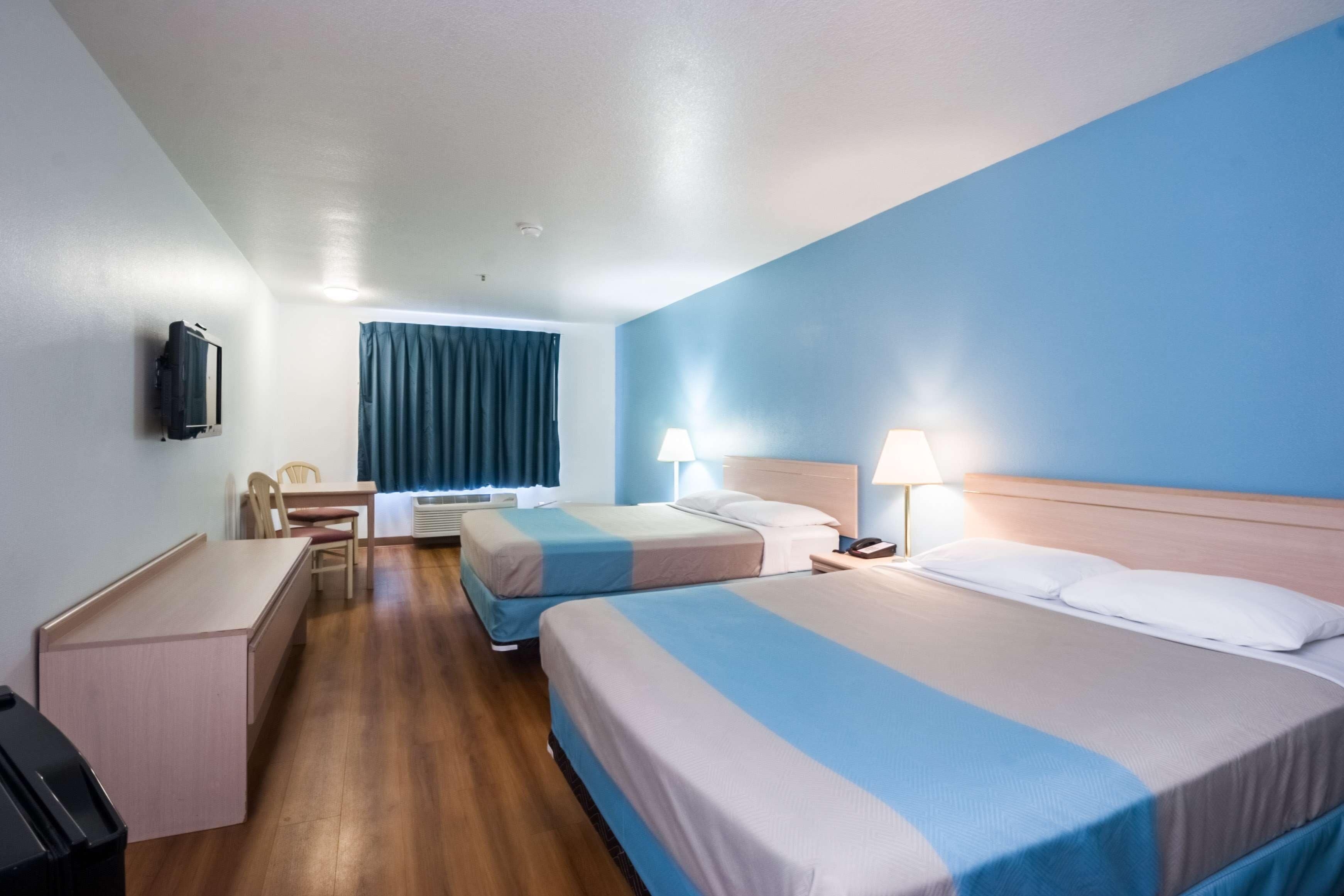 Une chambre d’hôtel avec deux lits, un bureau, une chaise, une télévision et une fenêtre avec des rideaux.