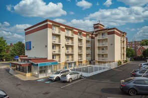 A multi-story hotel with a parking lot, a small entrance kiosk, and a clear sky. - Motel 6 Washington, DC (Washington)