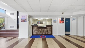 A reception area with a reception desk, a blue mat with a logo, and a staircase leading to an upper level. - Motel 6 Washington, DC (Washington)