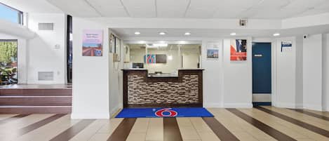 A reception area with a reception desk, a blue mat with a logo, and a staircase leading to an upper level.
