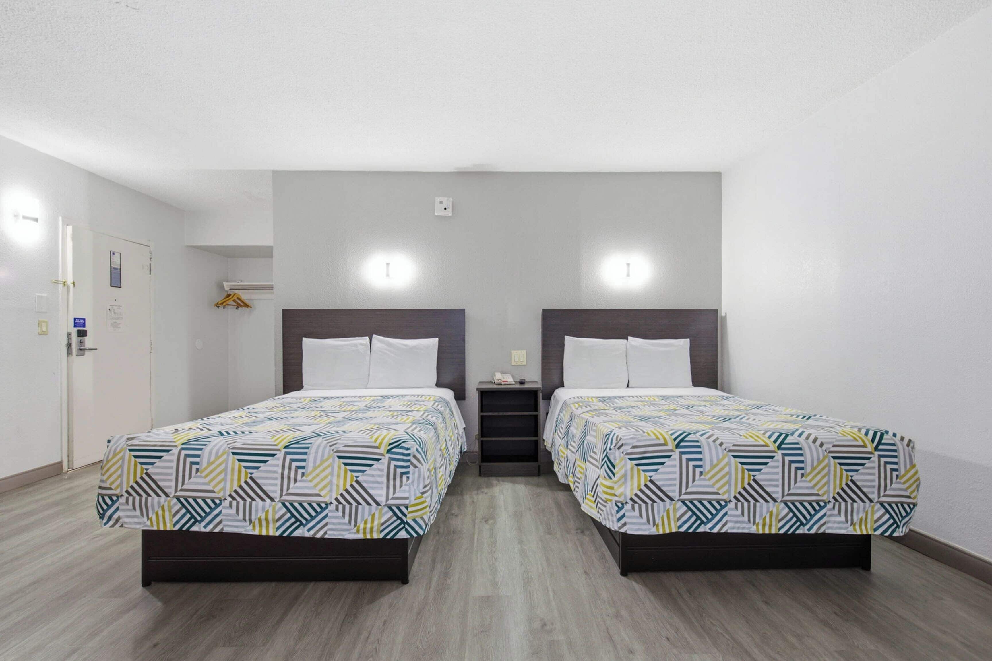 A hotel room with two beds, a small bedside table, a wall-mounted light, and a door with a handle.