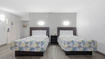 A hotel room with two beds, a small bedside table, a wall-mounted light, and a door with a handle.