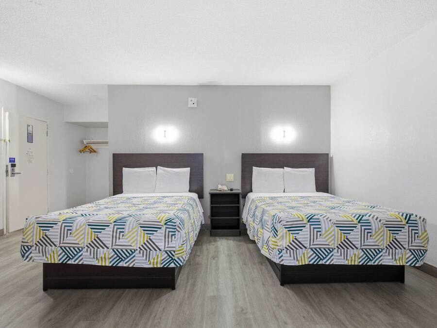 Camera d'albergo con due letti, un comodino, una lampada a parete e una porta con maniglia.