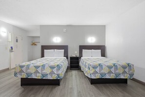 A hotel room with two beds, a small bedside table, a wall-mounted light, and a door with a handle. - Motel 6 Washington, DC (Washington)