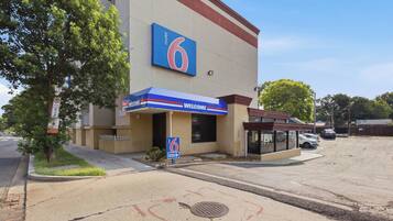 A motel with a large '6' sign, a 'WELCOME' entrance canopy, and a parking lot.
