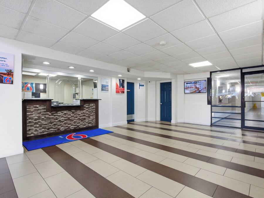 Un hall de hotel con una mesa de recepción, un felpudo azul con el símbolo de silla de ruedas y un suelo de baldosas con un diseño marrón y beige.