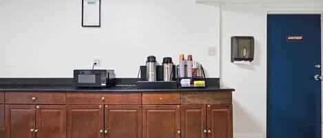 A kitchenette with a microwave, coffee maker, and coffee cups.