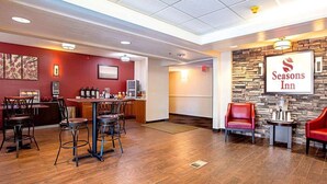 Un vestíbulo de hotel con zona de bar, sillas de cuero rojo y una pared de piedra con el logotipo de Seasons Inn.