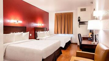 Een hotelkamer met twee bedden, een bureau, een stoel, een lamp en een raam met gordijnen.