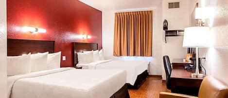A hotel room with two beds, a desk, a chair, a lamp, and a window with curtains.