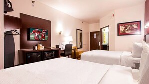 Habitación de hotel con dos camas, un escritorio con televisión, una lámpara y un pequeño rincón de descanso.