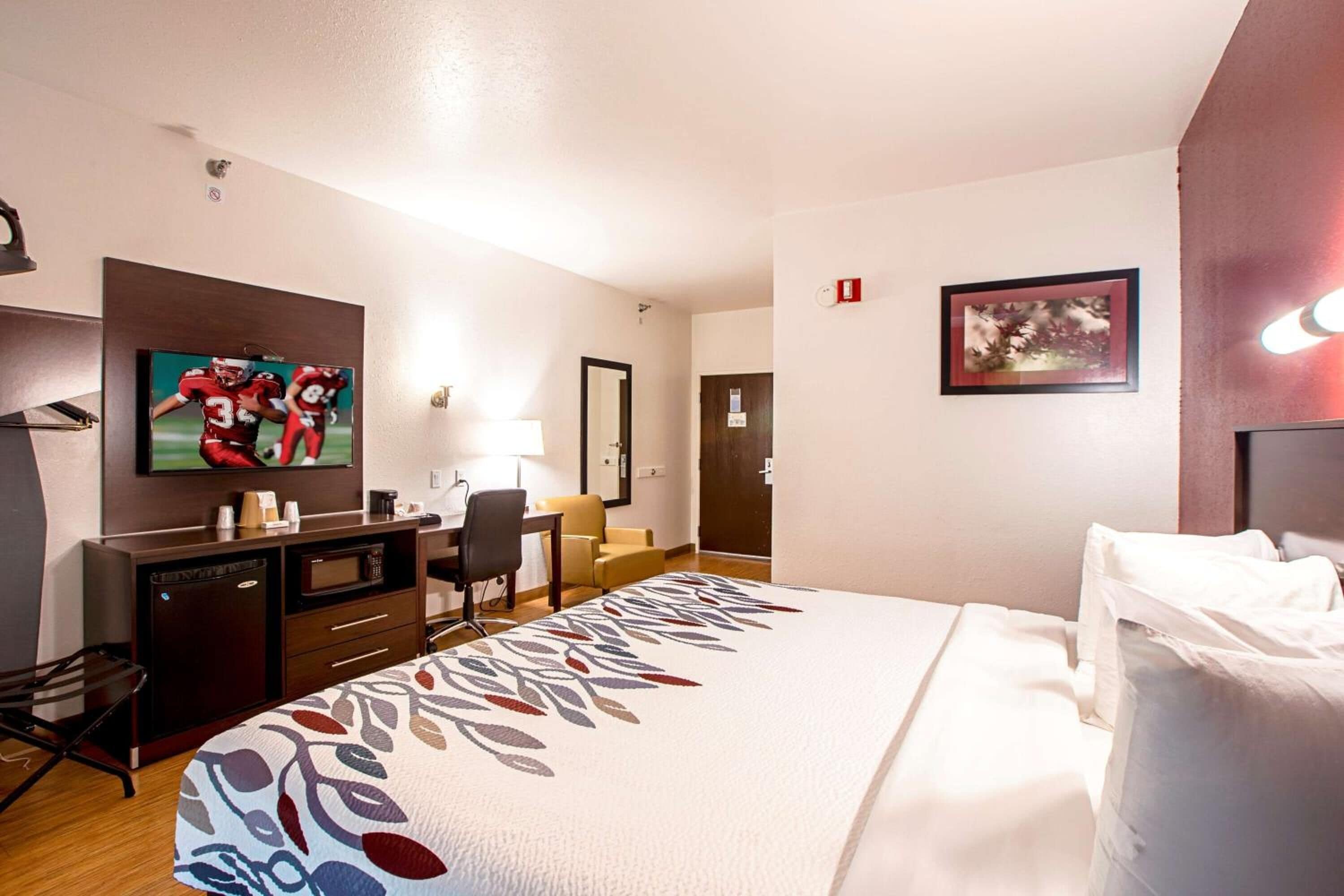A hotel room with a bed, a desk, a television, a microwave, and a dresser.