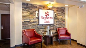 Vestíbulo de Seasons Inn con una pared de piedra, dos sillones de cuero rojo, una mesita con dispensador de agua y un letrero sobre la pared.