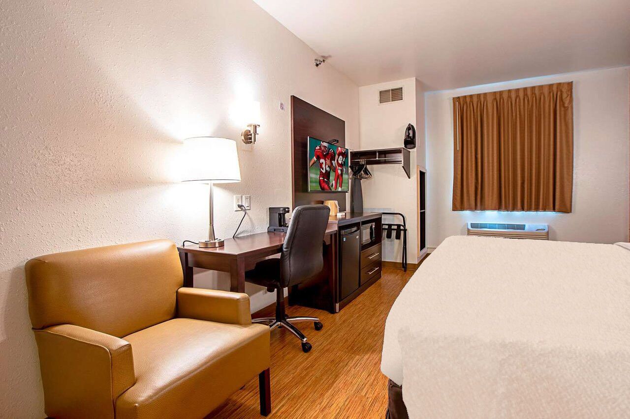 A hotel room with a bed, a desk with a chair, a lamp, a television, and a window with curtains.