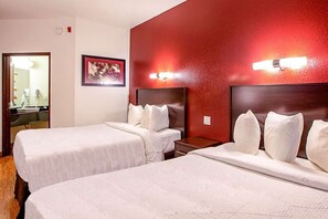 A hotel room with two beds, a red accent wall, and a framed artwork above the beds.