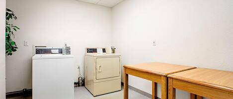 A laundry room with a washing machine, dryer, and a small cabinet. There is a wooden table and a brown rug on the floor.