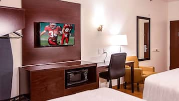 A hotel room with a bed, a desk with a television displaying football players, a microwave, a chair, and a lamp.