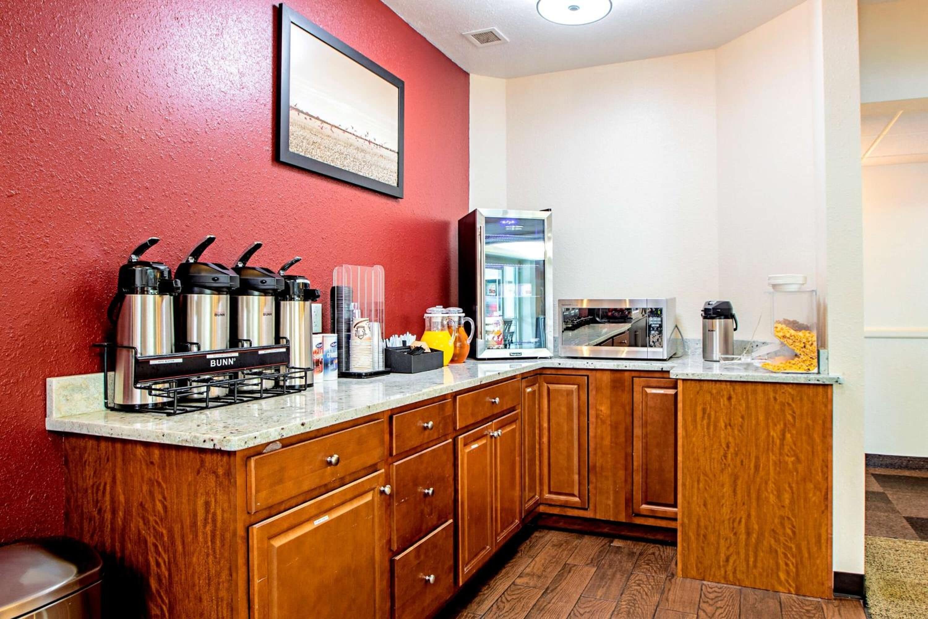 A compact kitchen with wooden cabinets, a coffee station, a microwave, and a refrigerator.