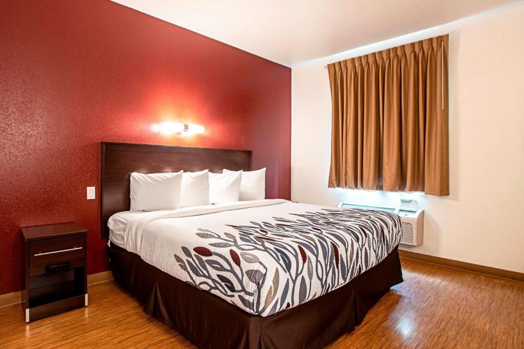 A hotel room with a large bed, a nightstand, a wall-mounted lamp, and a window with curtains.