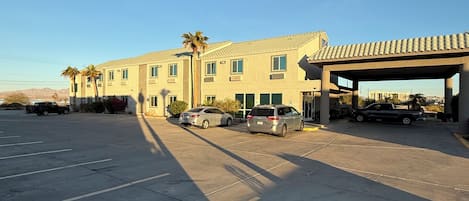A hotel with a parking lot, several cars, and a palm tree.