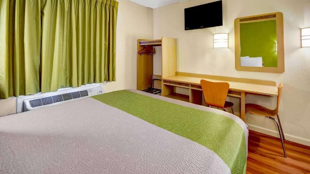 Una habitación de hotel con cama, escritorio, silla, televisor y espejo.