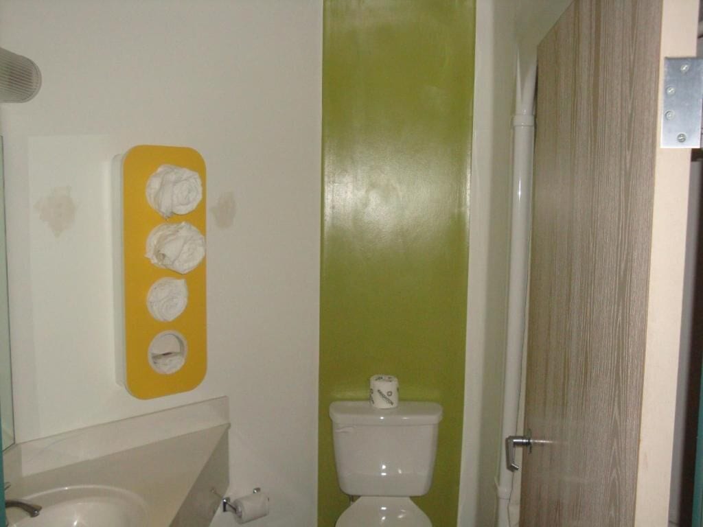 Une salle de bain avec des toilettes, un lavabo et un distributeur de savon jaune fixé au mur.