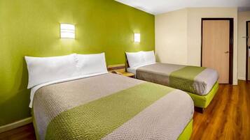 Quarto de hotel com duas camas, paredes verdes e piso de madeira.