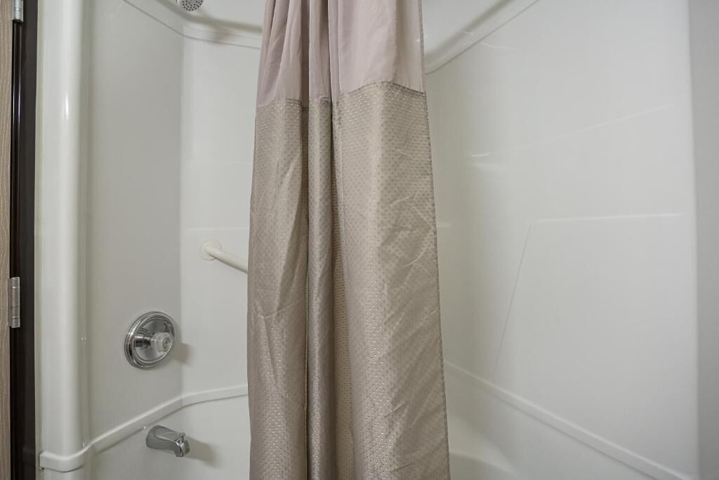 A shower area with a beige shower curtain, a chrome faucet, and a wall-mounted control panel.