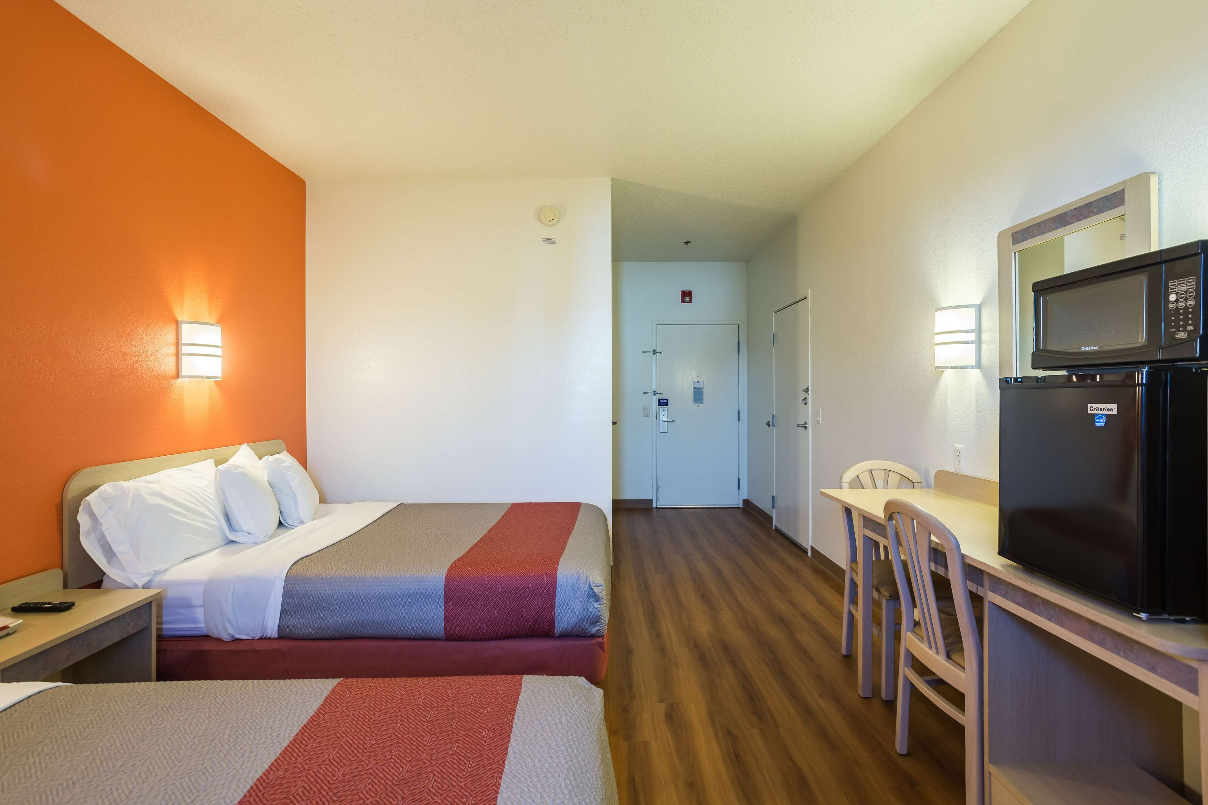 A hotel room with two beds, a desk, a microwave, and a dining area.