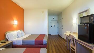 A hotel room with two beds, a desk, a microwave, and a dining area.