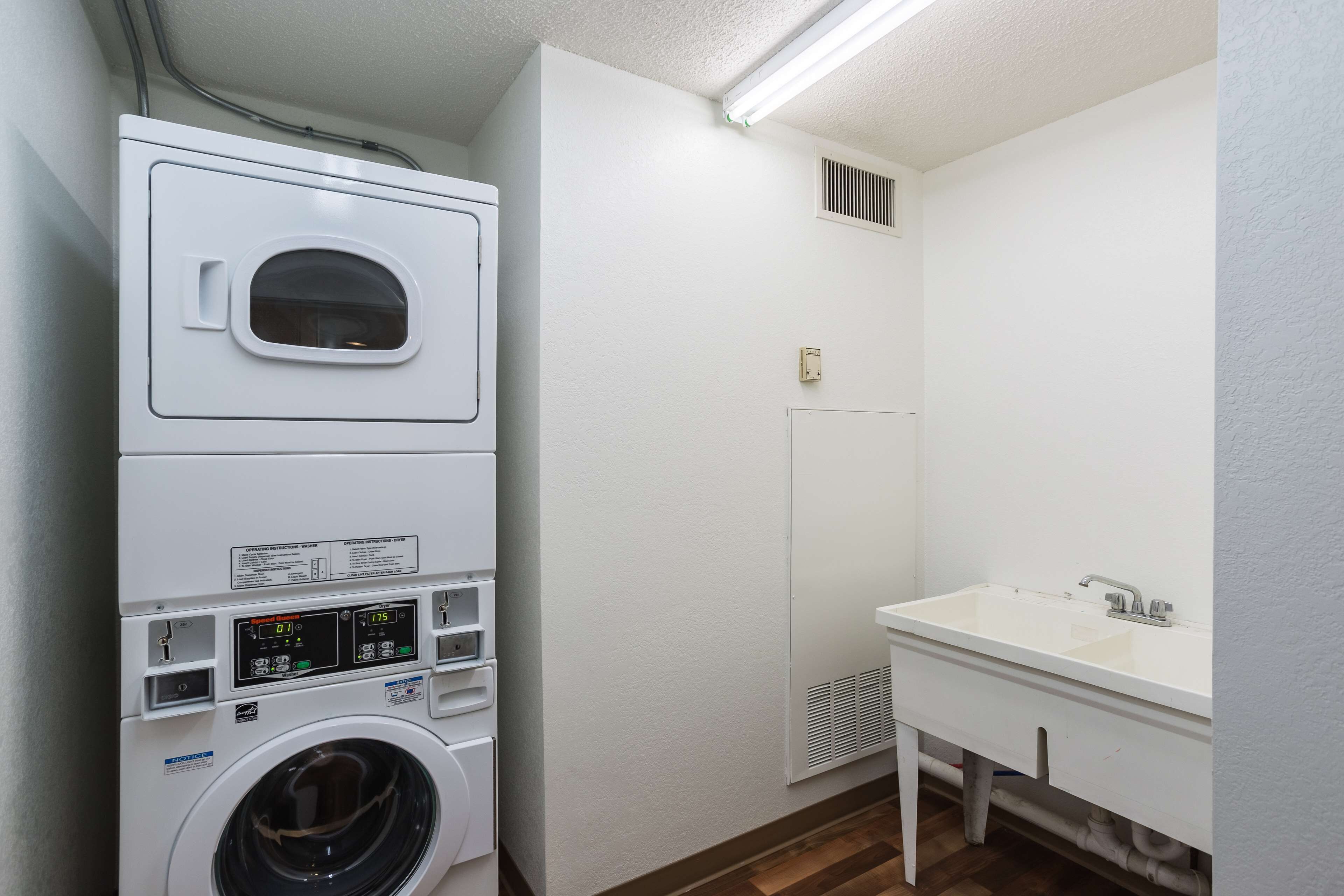 A laundry room with stacked washers and dryers, a sink, and a vent.
