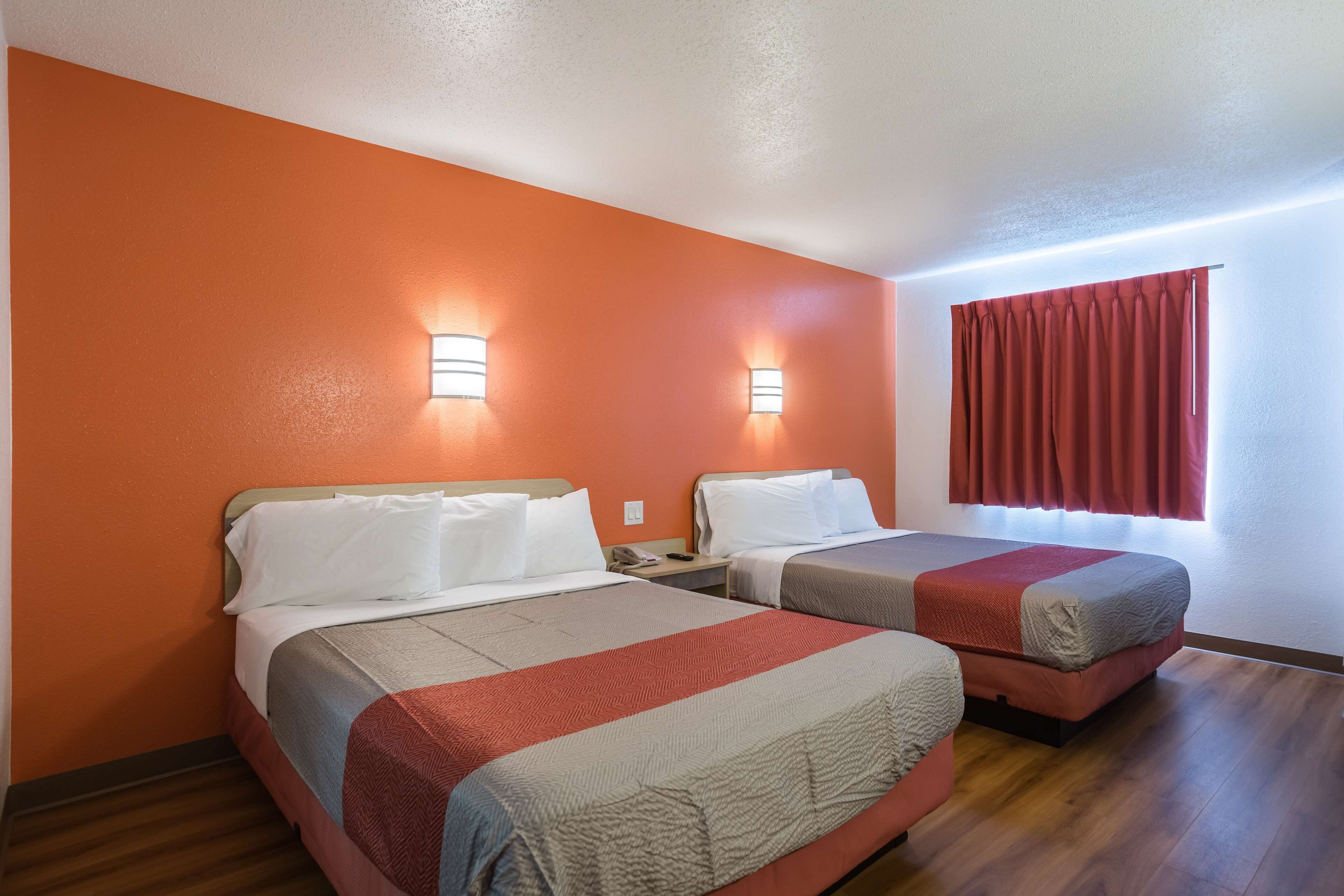A hotel room with two beds, orange walls, and a window with red curtains.