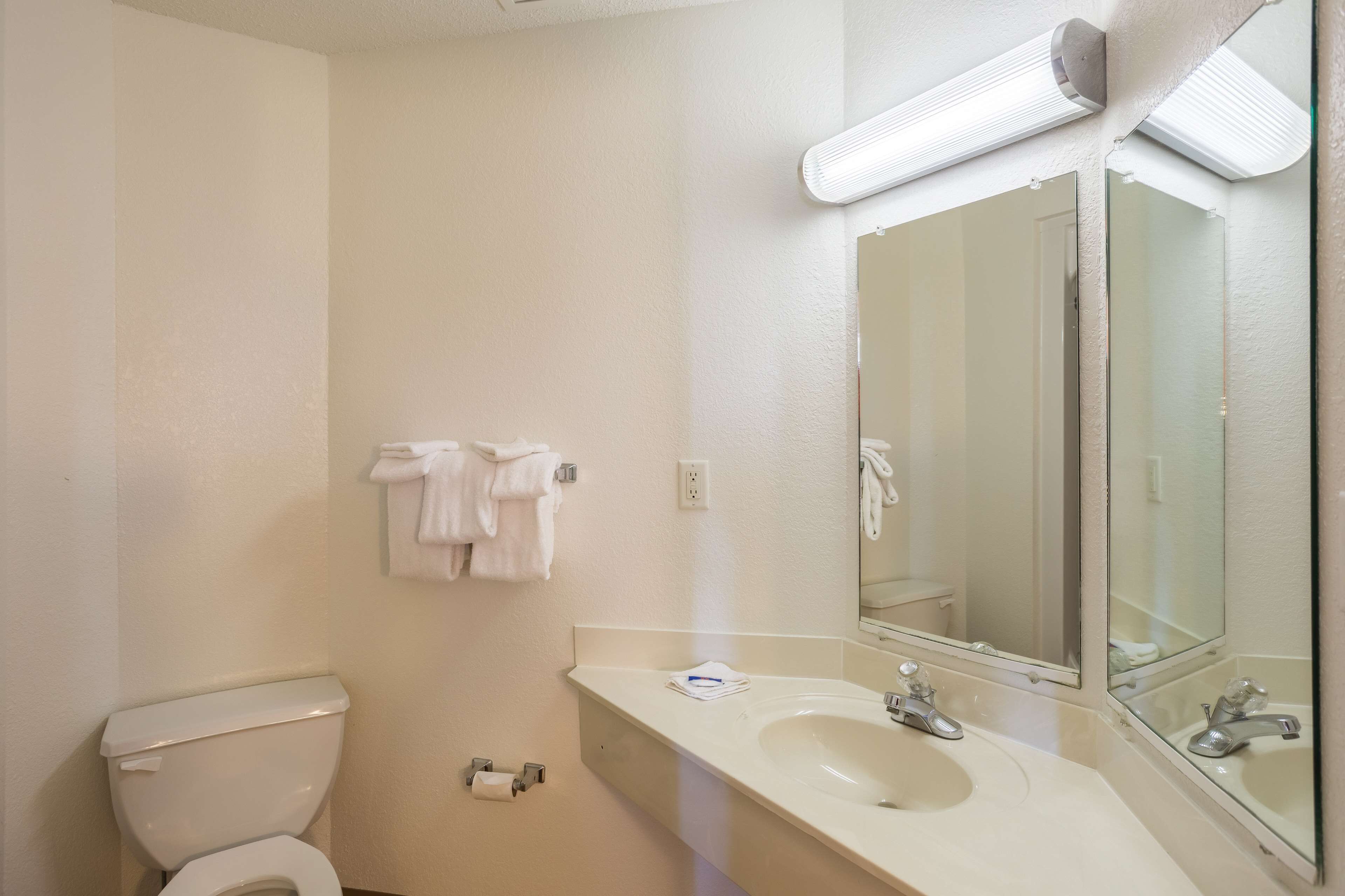 A bathroom with a toilet, sink, mirror, and towel rack.