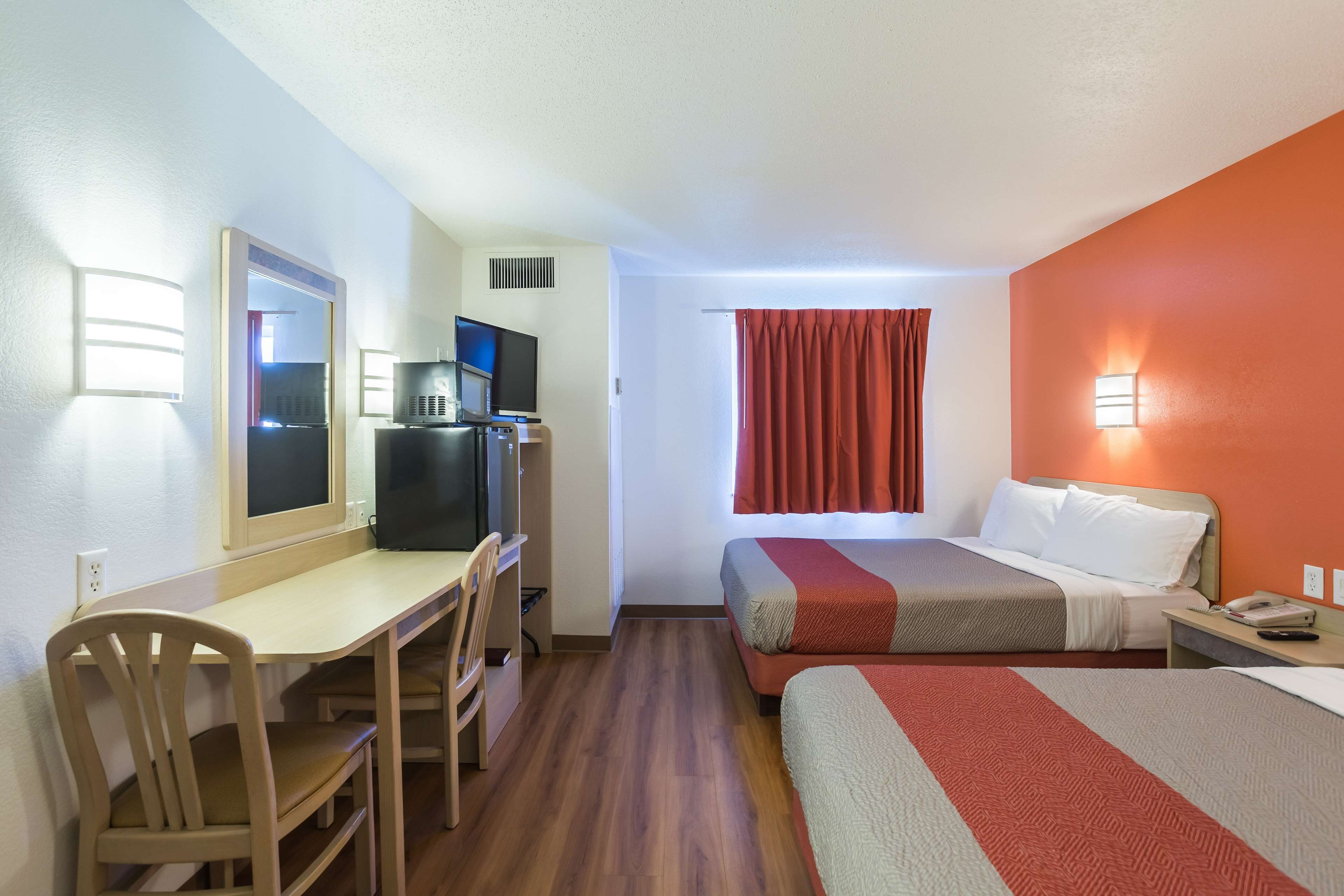 A hotel room with a desk, two beds, a TV, and a window with curtains.