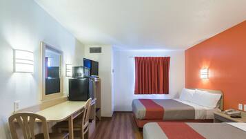 A hotel room with a desk, two beds, a TV, and a window with curtains.