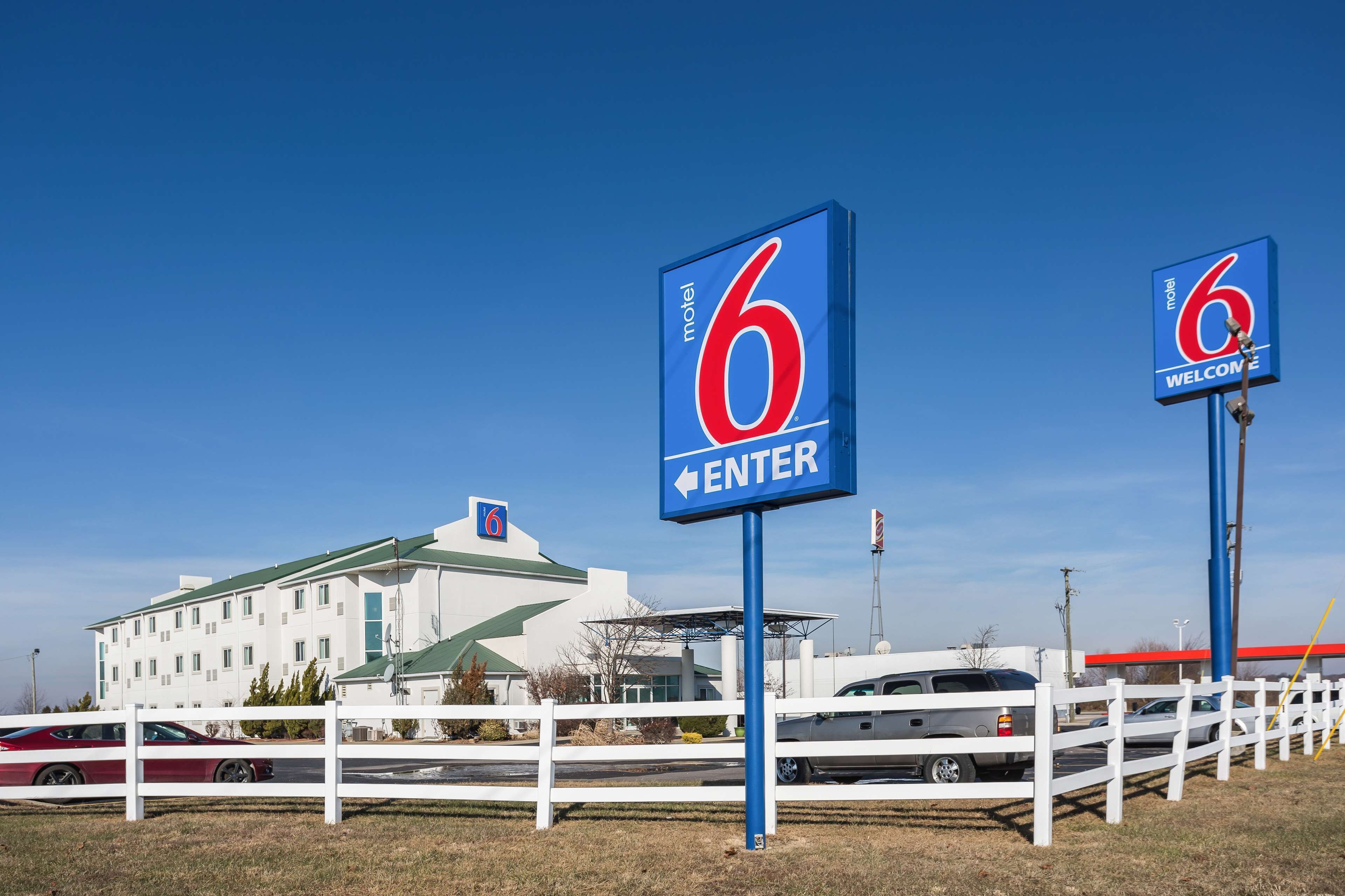Een motel met een groot bord waarop '6' staat, een wit hek en een gebouw met een groen dak.