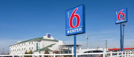 Een motel met een groot bord waarop '6' staat, een wit hek en een gebouw met een groen dak.