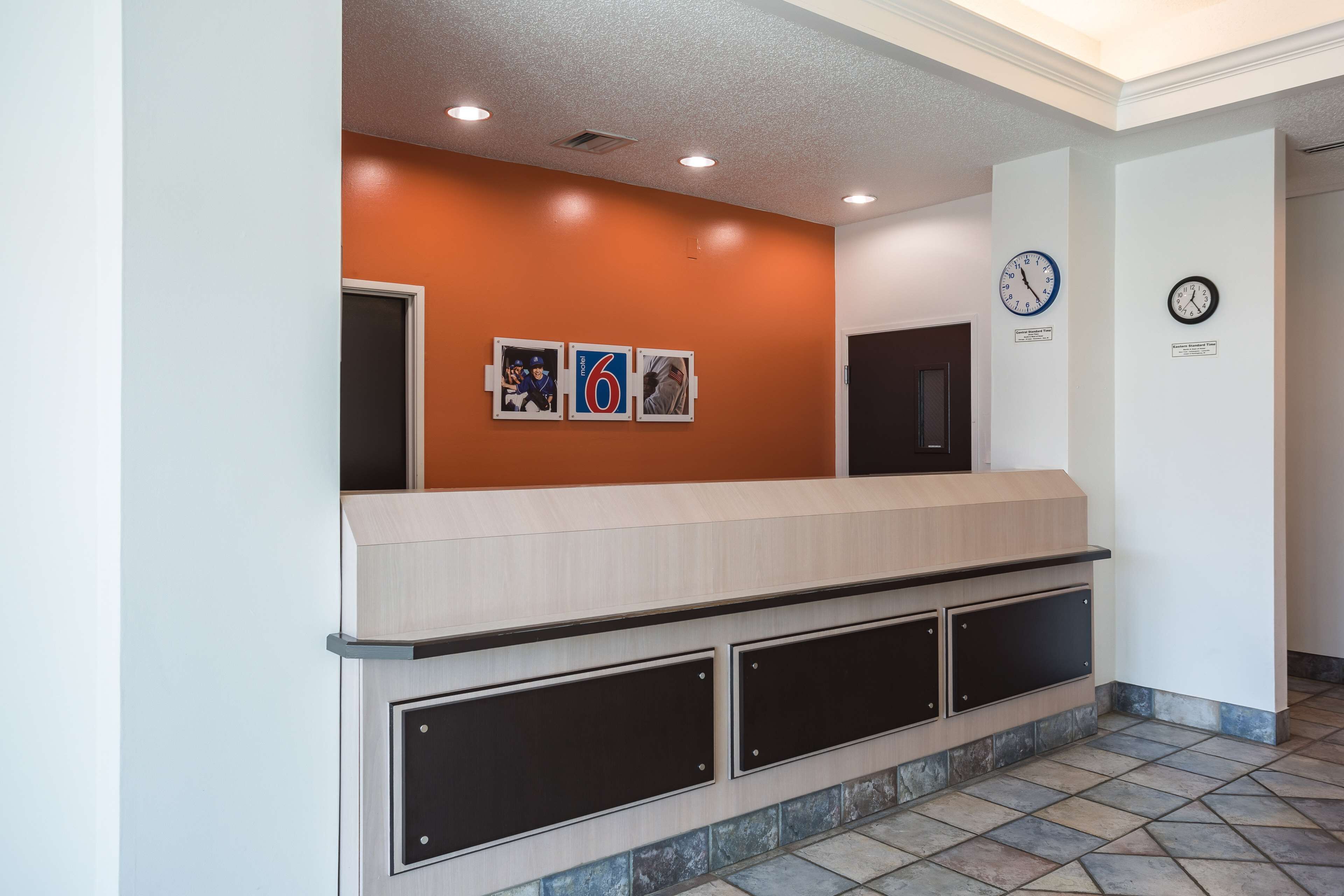 A reception area with a wooden counter, two clocks, and three framed photos on the wall.