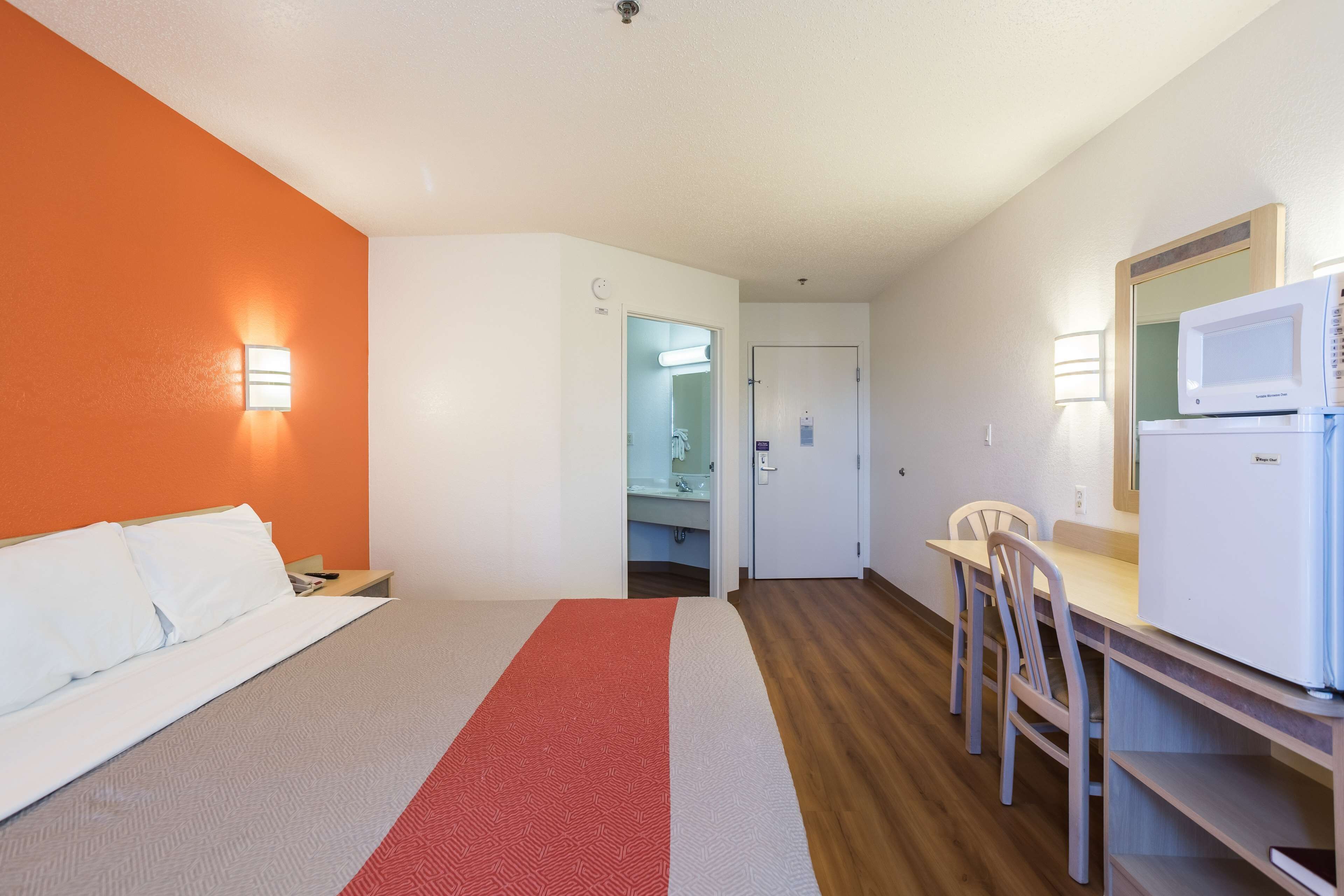 A hotel room with a bed, a desk with a chair, a microwave, and a bathroom visible through an open door.