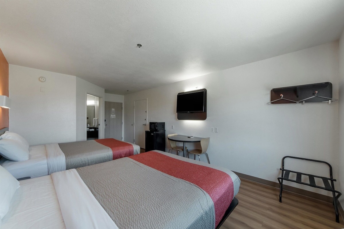 Une chambre d’hôtel avec deux lits, un bureau, une chaise, un téléviseur fixé au mur et un porte-manteau.