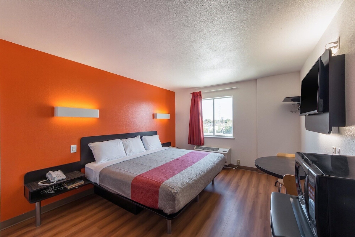 Une chambre d’hôtel avec un lit, une table de chevet, une télévision et une fenêtre avec des rideaux.