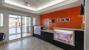 A hotel reception area with a glass door entrance, a reception desk, and a wall with framed pictures and a motivational poster.