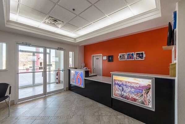 A hotel reception area with a glass door entrance, a reception desk, and a wall with framed pictures and a motivational poster.