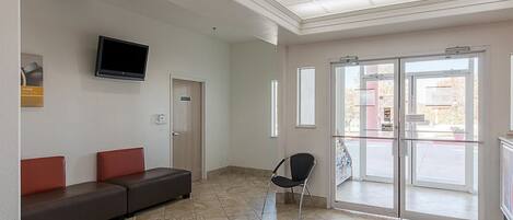 Un vestíbulo con zona de estar, televisor, puerta con un letrero y puerta de cristal que da al exterior.