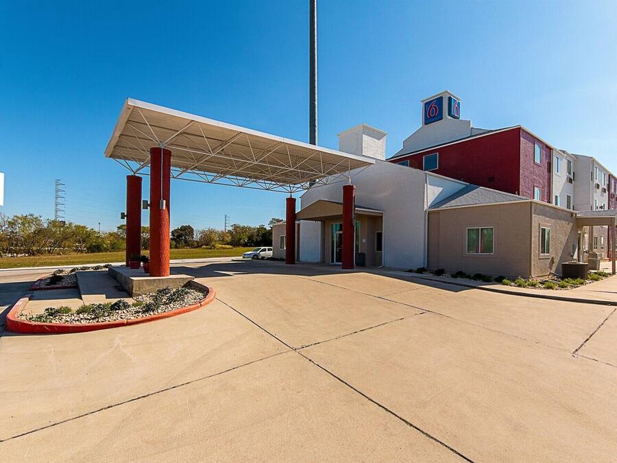 Un hotel moderno con una gasolinera techada, un edificio rojo y blanco, y un cielo azul despejado.