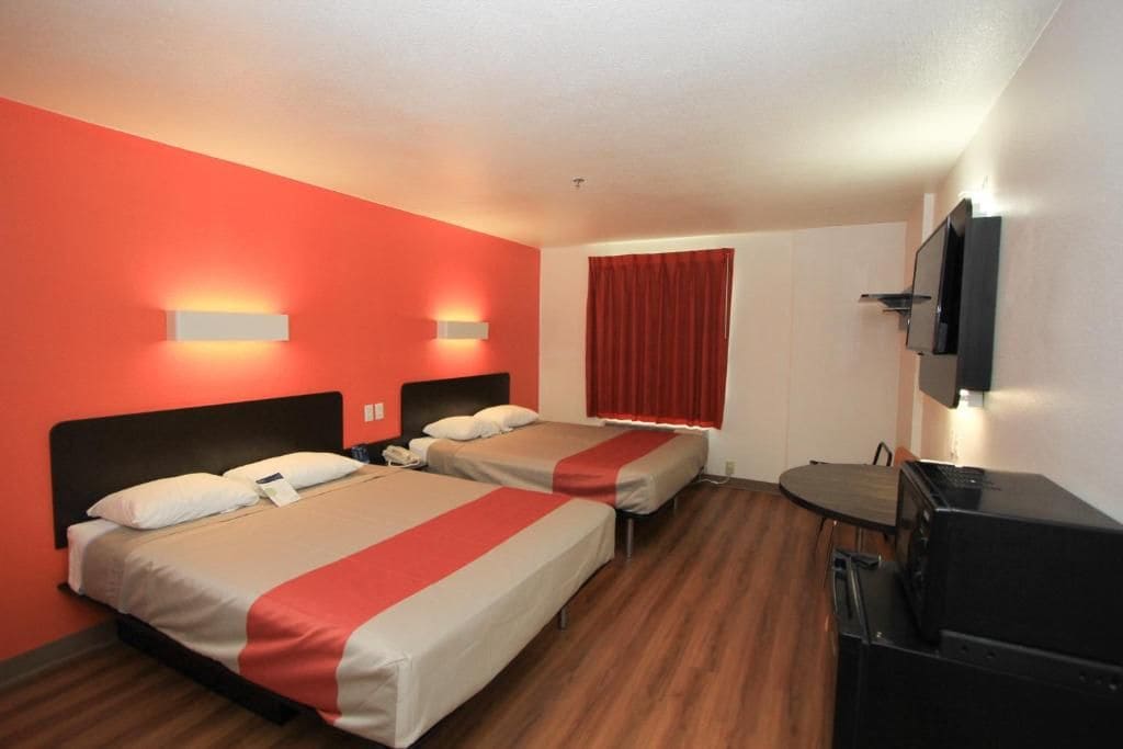 Una habitación de hotel con dos camas, un escritorio, un televisor y una cortina roja.