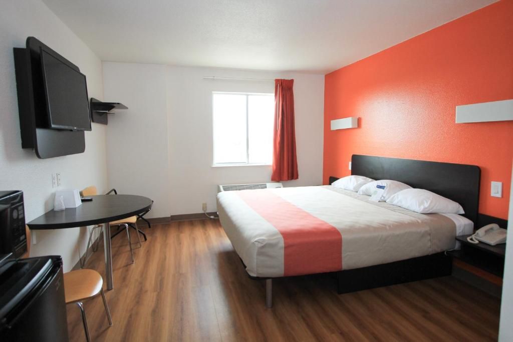 A hotel room with a bed, a desk, a chair, a television, and a window with curtains.