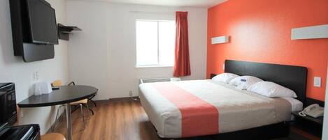 A hotel room with a bed, a desk, a chair, a television, and a window with curtains.