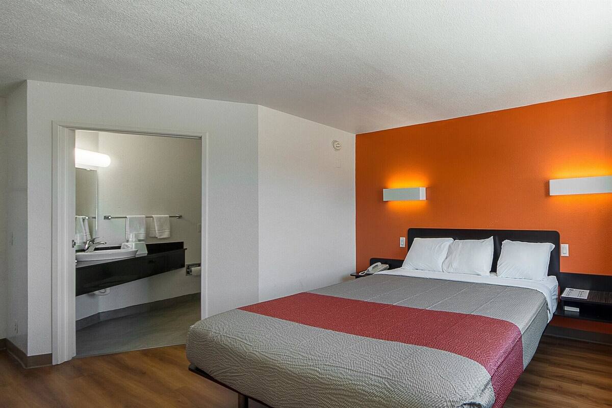 Une chambre d’hôtel avec un lit, une table de chevet, une commode et une salle de bain visible à travers une porte ouverte.
